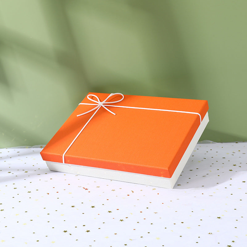 Orange box package for suit set accessories with white ribbon on star-patterned surface