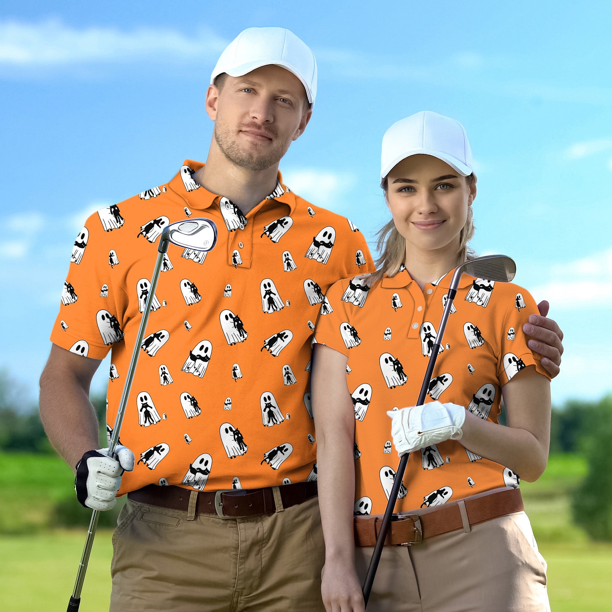 Couple wearing matching orange golf shirts with Halloween ghost and cat hug pattern, holding golf clubs outdoors.