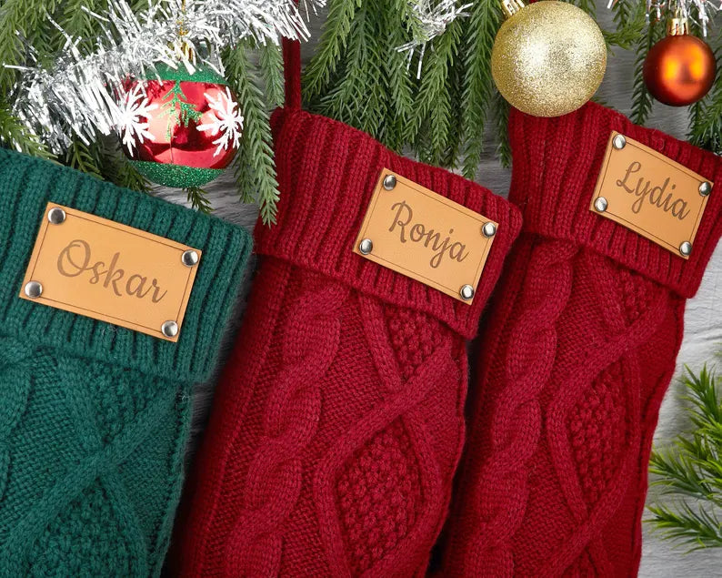 Engraved leather Christmas stockings with personalized names hanging on festive pine branches