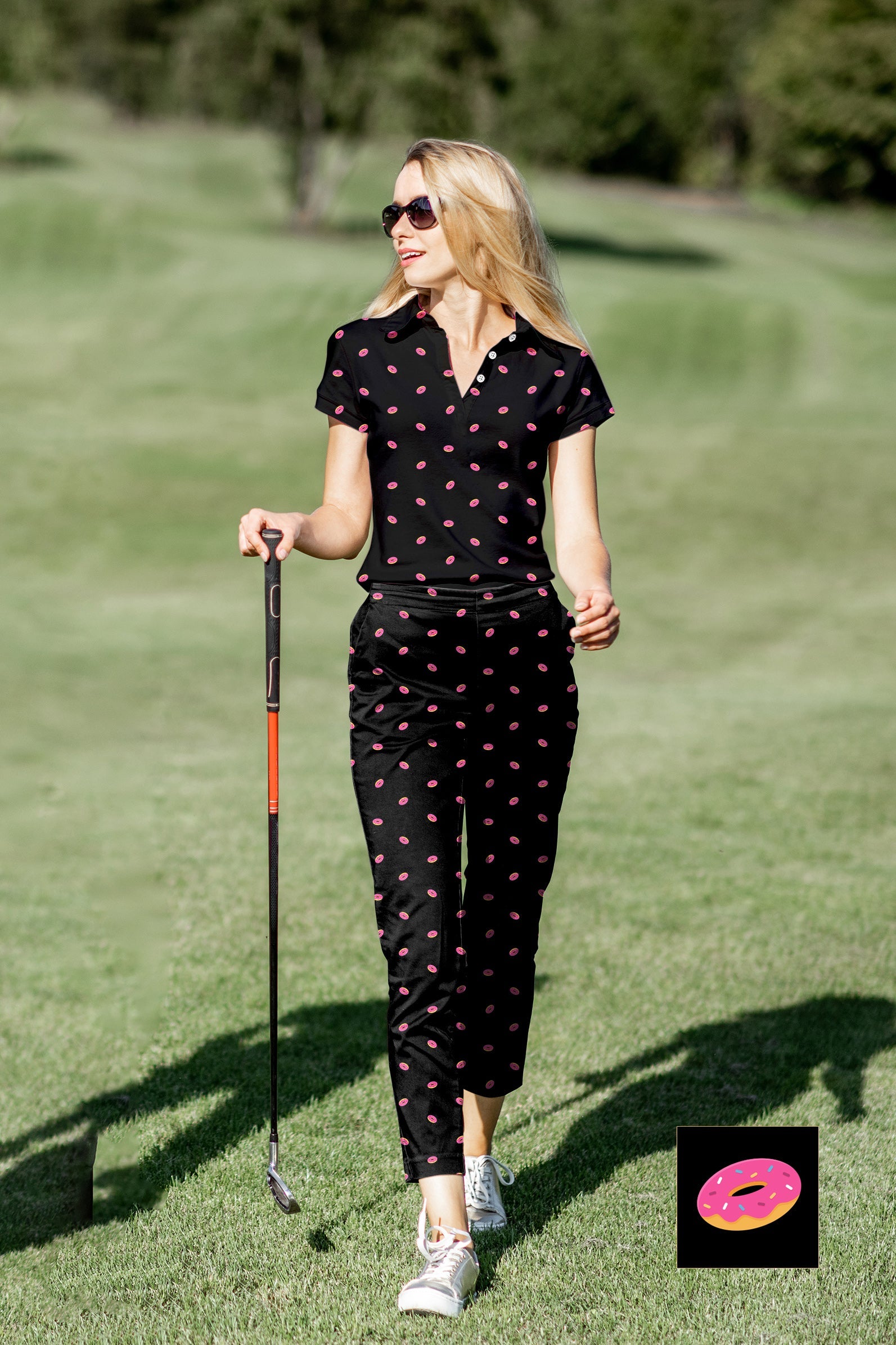 Woman wearing black women's golf polo with pink donut pattern and matching pants on golf course
