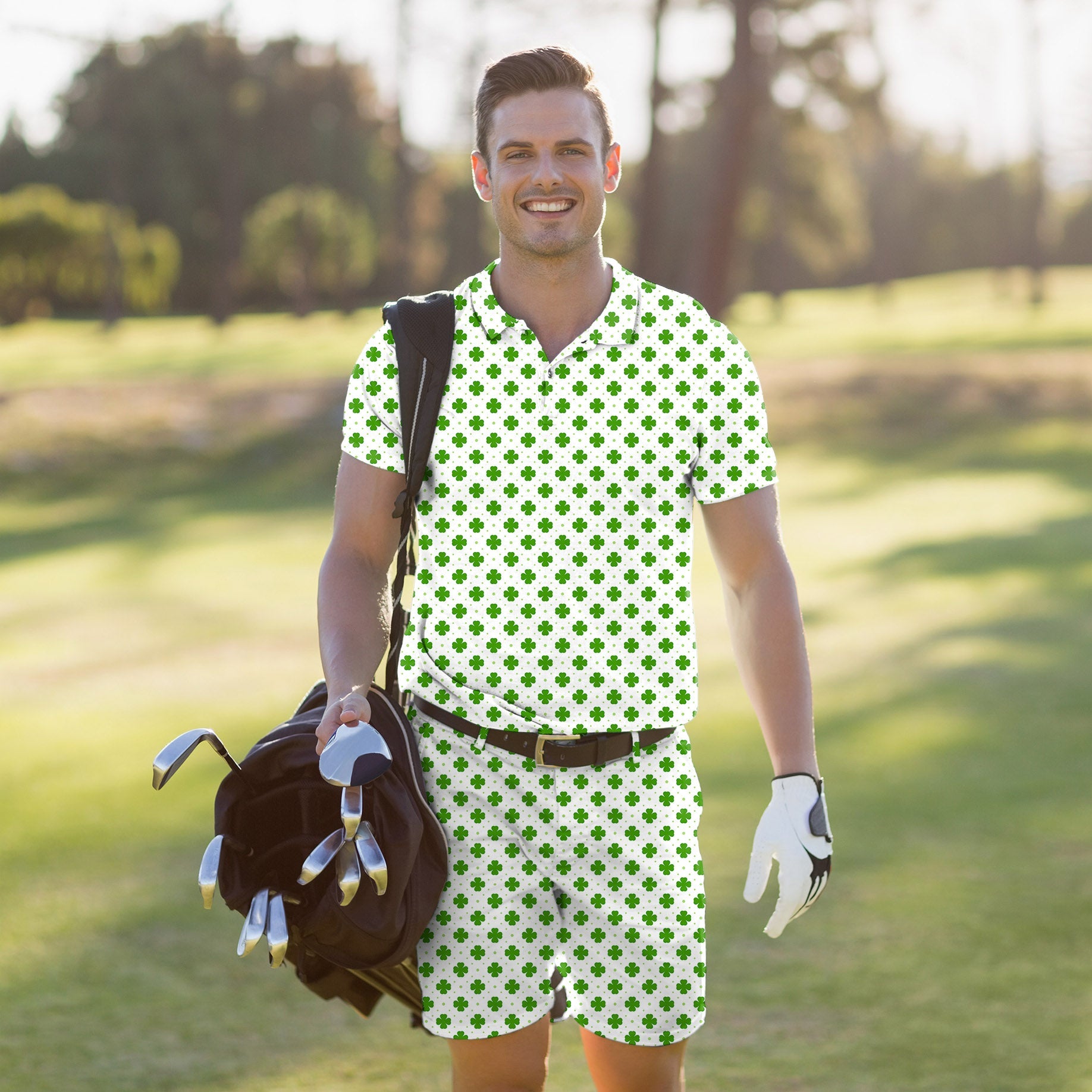 Men's golf set polo and shorts with green leaf clover pattern for St. Patrick's Day on a smiling golfer carrying clubs.
