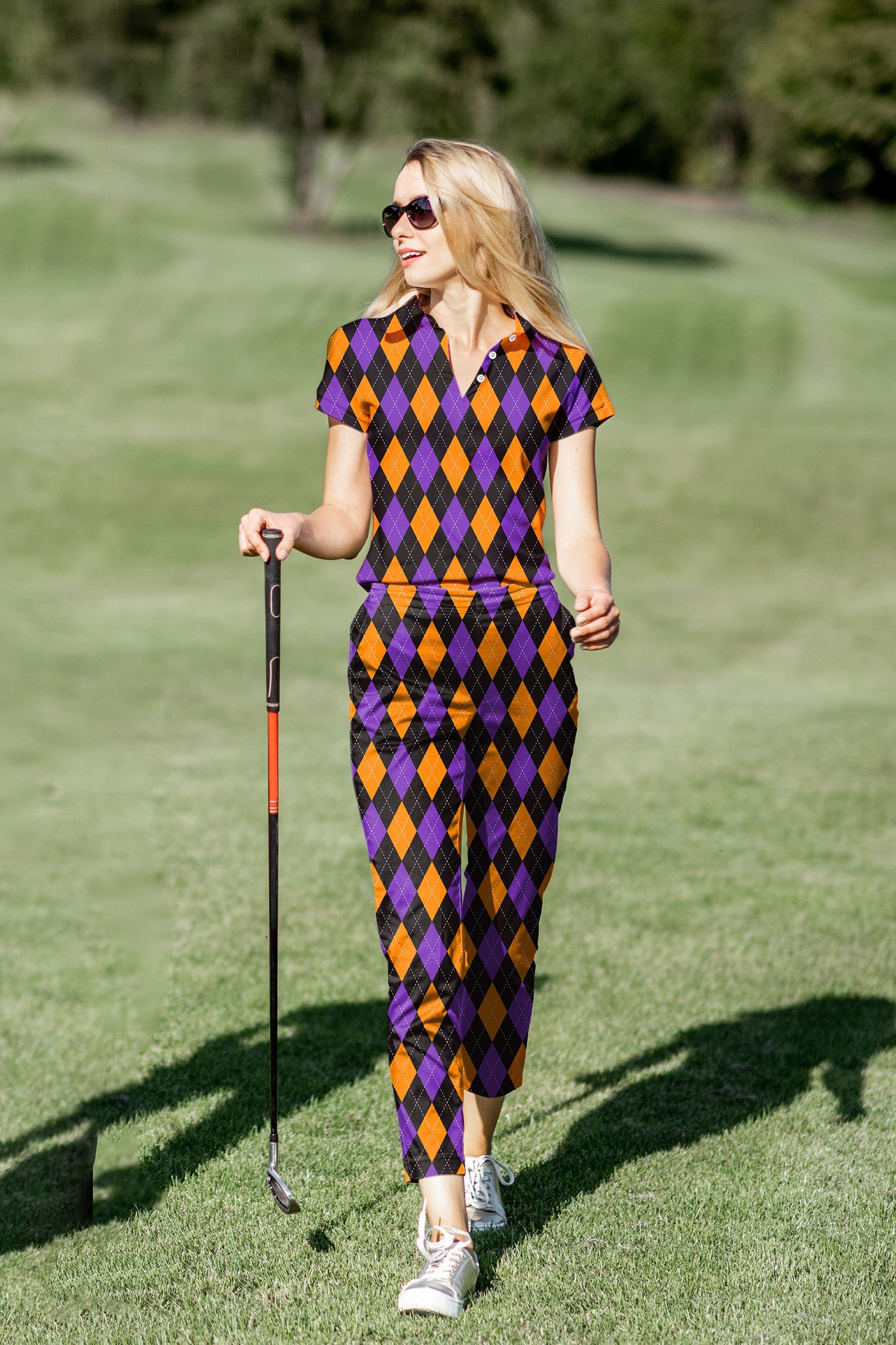 Women's golf polo and pants set with orange, purple, and black argyle pattern on golf course