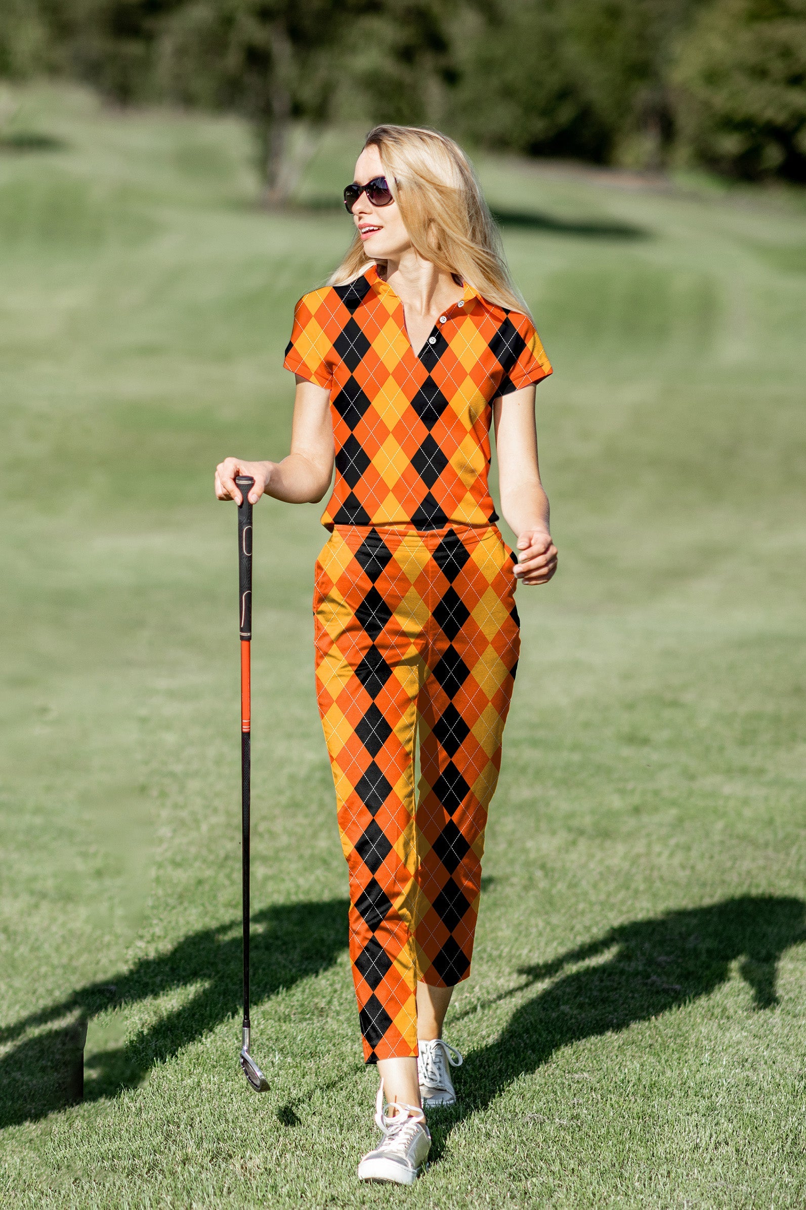 Woman wearing Halloween-themed black, yellow, and orange argyle women's golf polo and pants set on golf course