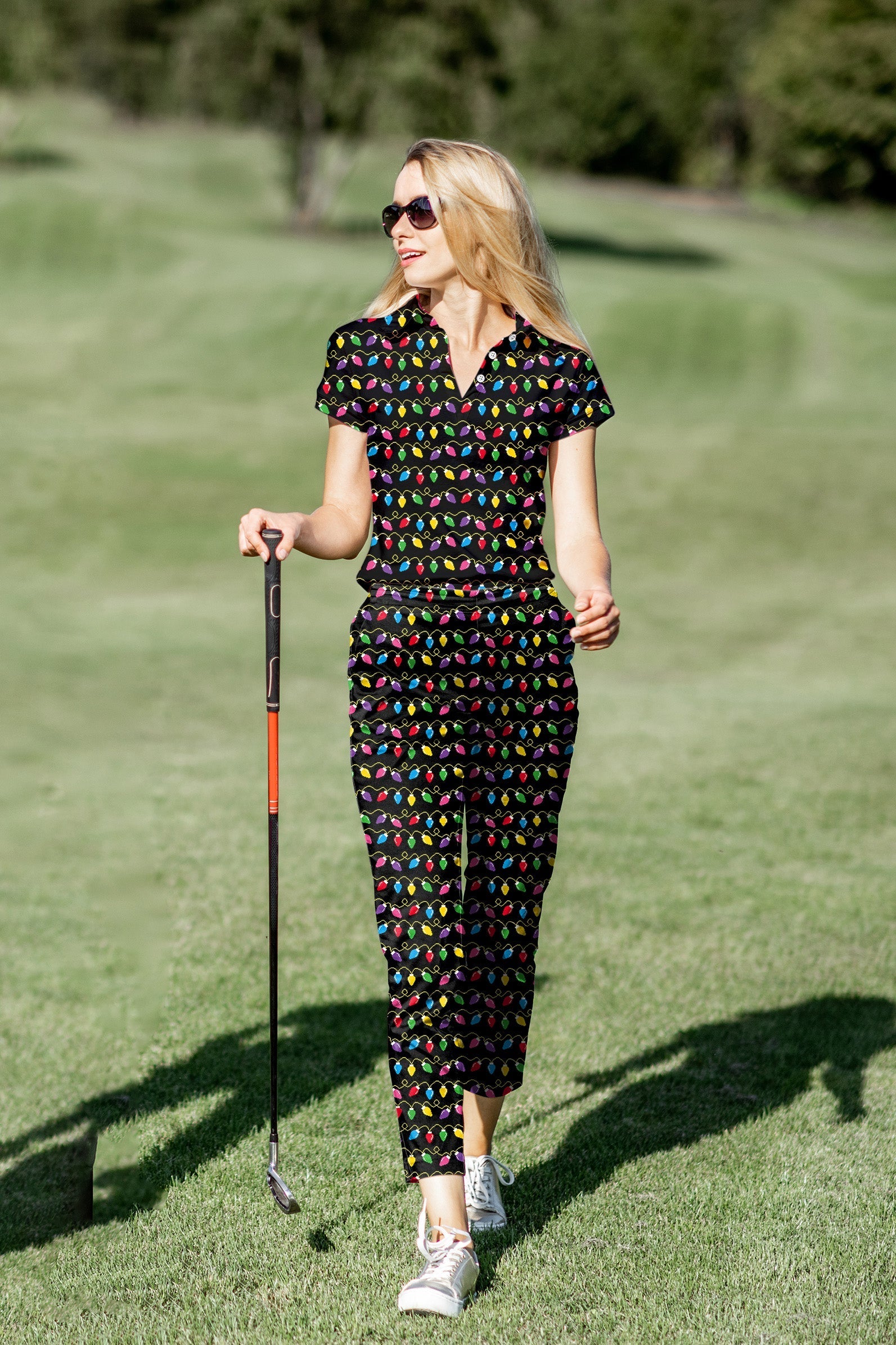 Woman wearing a colorful Christmas lights patterned women's golf polo and pants set on a golf course