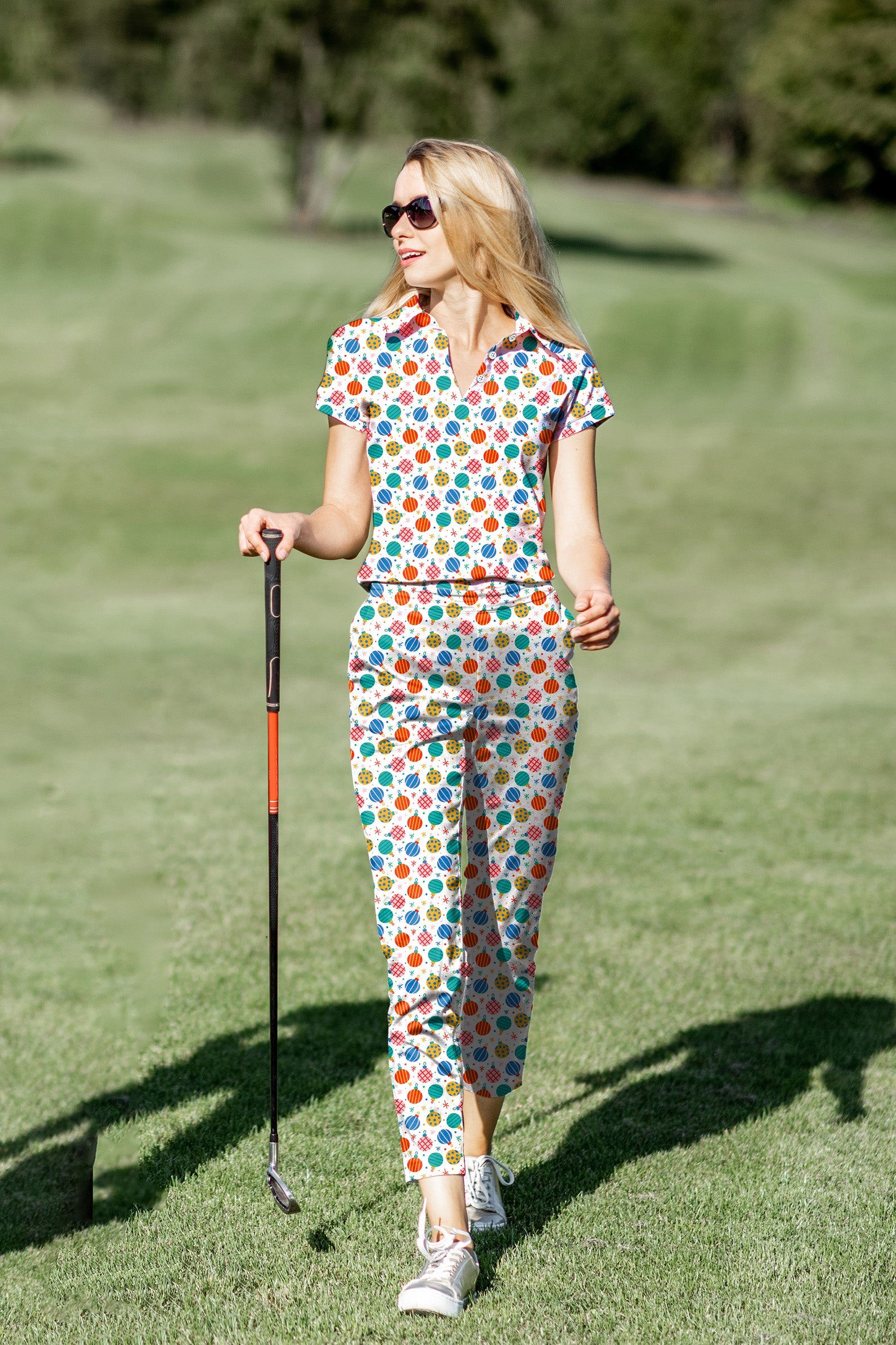 Woman wearing colorful Christmas-themed women's golf polo and pants set on golf course
