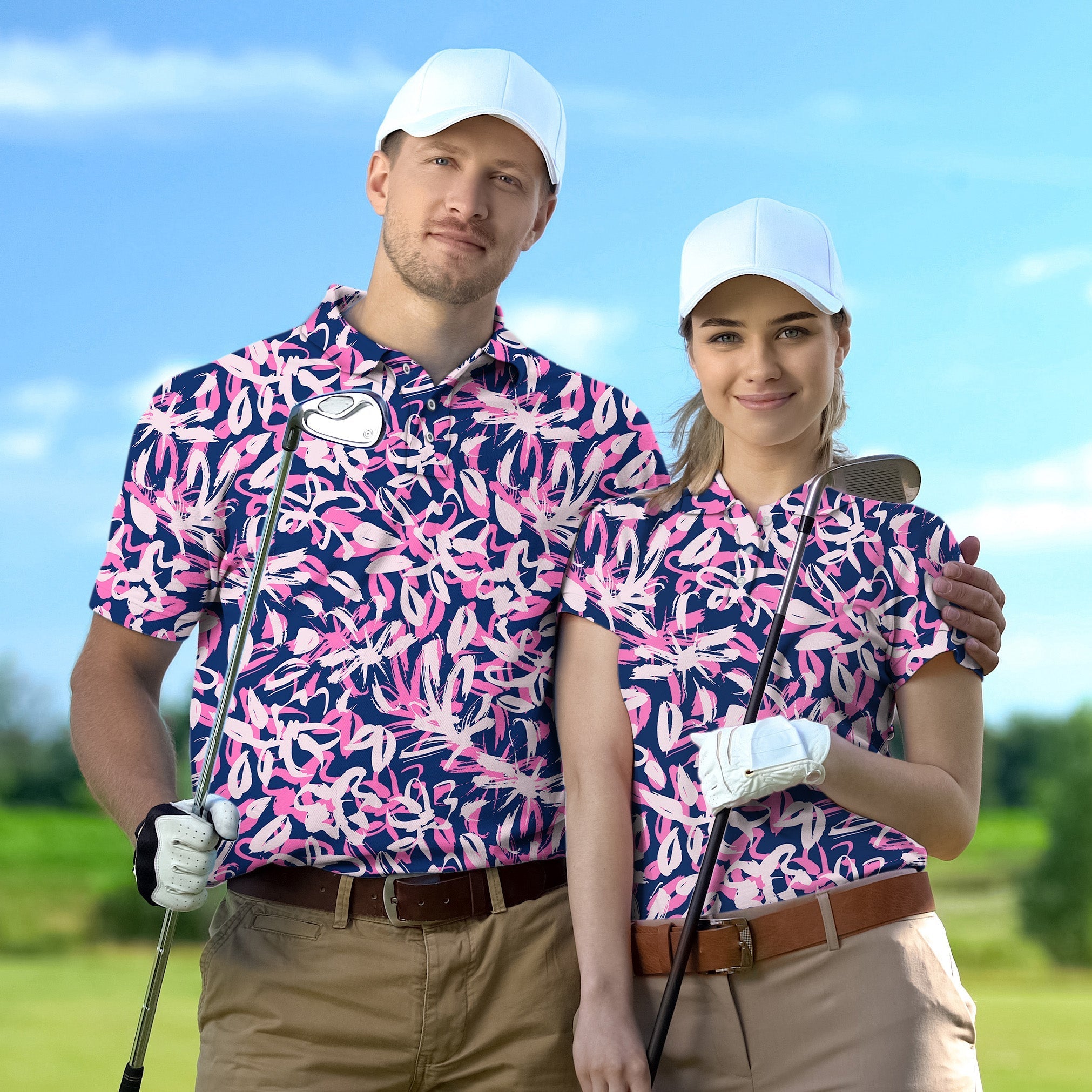 Couple wearing matching pink and navy floral golf shirts with white caps on golf course holding clubs