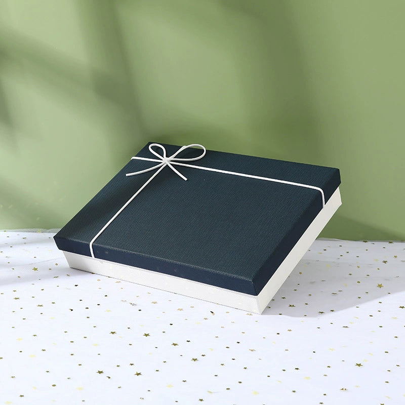 Suit set accessories box package with navy lid and white base tied with white string bow on patterned surface